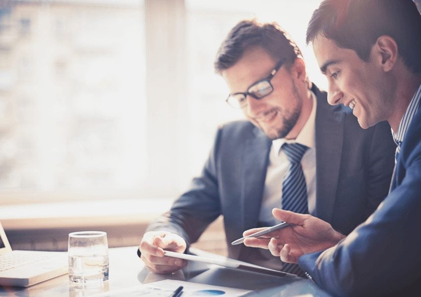 Two men in suits discussing something on a tablet