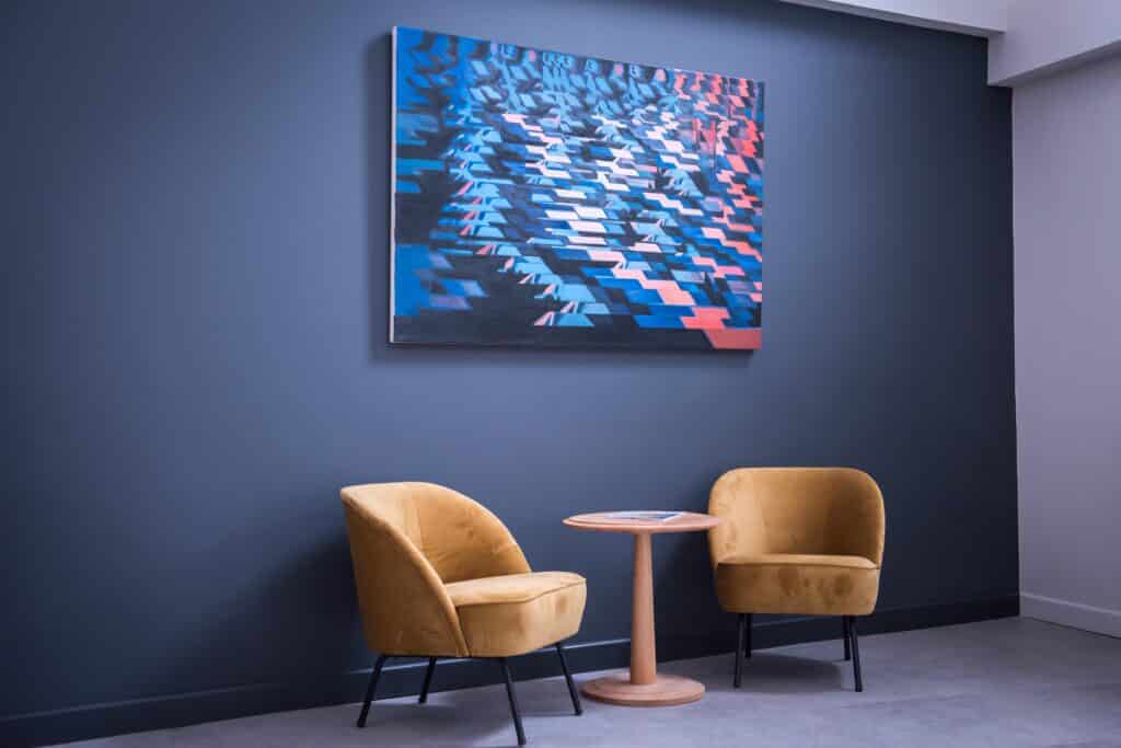 Two yellow chairs with a table and art hanging above on the wall