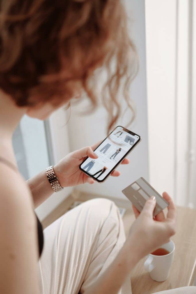 Female looking at clothing shop on mobile device and holding a card to purchase.