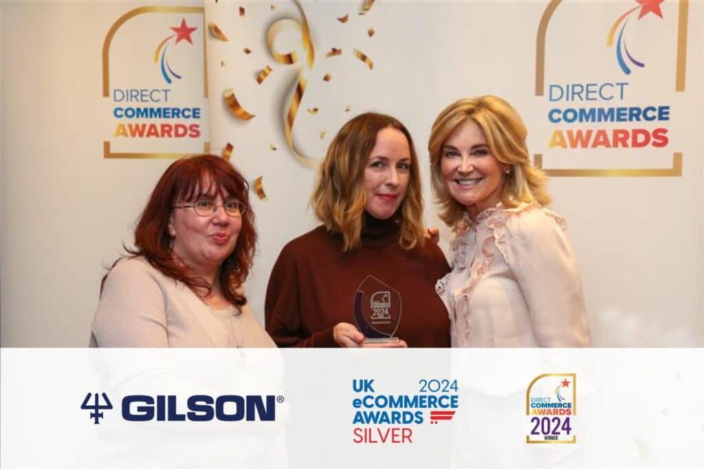 Tanya Peasgood, Kathryn Fletcher and Anthea Turner at Direct Commerce Awards featuring a banner with Gilson's logo, UK Ecommerce Awards Silver logo and Direct Commerce Awards logo