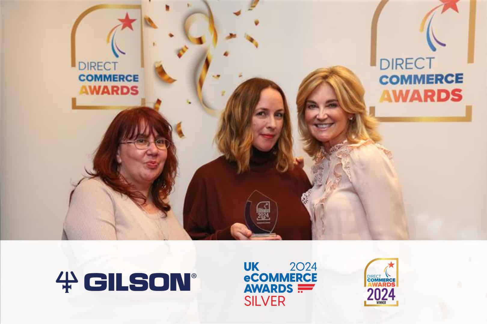 Tanya Peasgood, Kathryn Fletcher and Anthea Turner at Direct Commerce Awards featuring a banner with Gilson's logo, UK Ecommerce Awards Silver logo and Direct Commerce Awards logo